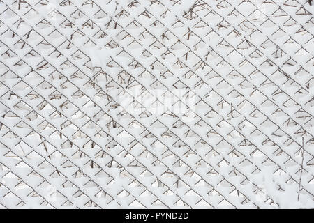 Close-up pattern of many cells of chain-link fence that are covered with bright white fresh snowin light of winter morning. Stock Photo