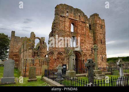 Front of Lindisfarne church ruins of the medieval priory with rainbow arch and cemetery tombstones on Holy Island of Lindisfarne England UK Stock Photo
