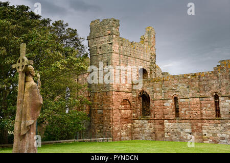 Life size statue of St Aidan first bishop of Lindisfarne facing ruins of the medieval priory on Holy Island of Lindisfarne England UK