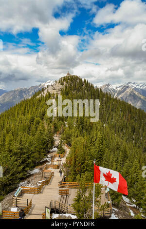 BANFF, AB, CANADA - JUNE 2018: National flag of Canada, the Maple Leaf, flying on Sulphur Mountain in Banff. In the distances is the old meteorologica Stock Photo