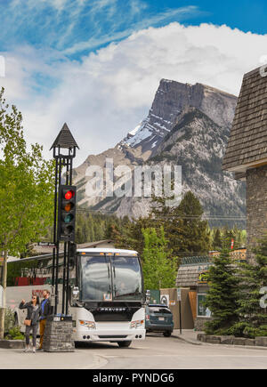 BANFF, AB, CANADA - JUNE 2018: Tour bus parked in a side street in Banff town centre with high mountain peak in the background. Stock Photo
