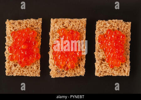 Three sandwiches, canapes with natural red salmon caviar on a dark board, top view Stock Photo