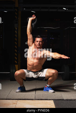 Athletic strong man doing the exercises with kettlebell on dark shadow background. Closeup contrast portrait. Stock Photo