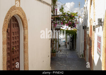 One of the many narrow streets of Lindos, a small fishing village very popular with tourists. The houses are coloured white and the village sits benea Stock Photo