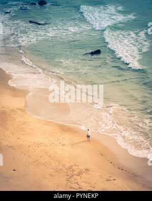 From above view of young man walking on beach along sea shore near water in Biarritz, France Stock Photo
