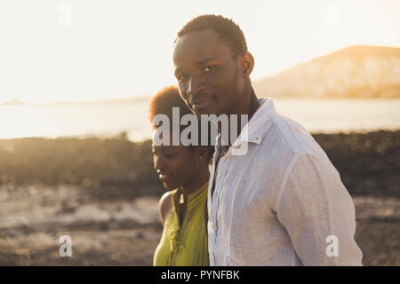 Romantic black race happy couple in love african young people walking together with ocean and beach in background enjoying the outdoor leisure activit Stock Photo