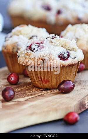 Cranberry Muffins with lemon sugar topping on a rustic cutting board with loose berries. Extreme shallow depth of field with selective focus on muffin Stock Photo
