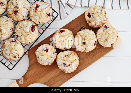 Fresh cranberry muffins cooling on a bakers rack and a wood cutting board over a rustic white table  background. Image shot from above with free space Stock Photo