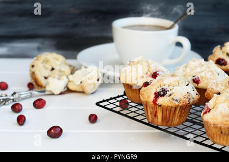 Cranberry Muffins cooling on a bakers rack with extreme shallow depth of field and open muffin with butter and a steaming hot cup of coffee in the bac Stock Photo