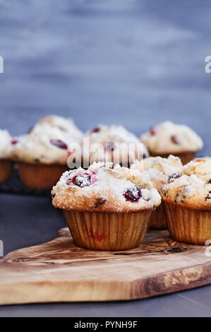 Cranberry Muffins with lemon sugar topping on a rustic cutting board with loose berries. Muffins on cooling rack in background. Extreme shallow depth  Stock Photo
