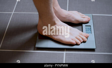 Male feet on glass scales, men's diet, body weight, close up, man standing on scale Stock Photo