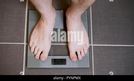 Male feet on glass scales, men's diet, body weight, close up, man standing on scales, top down view Stock Photo