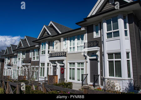 Row of new townhomes in a sidewalk neighborhood. On a sunny day in spring against bright blue sky. Stock Photo