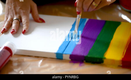 Female artist painting a rainbow with acrylic colors on canvas, hoe made art, DIY tutorial, colorful Stock Photo