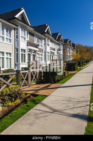 Row of new townhomes in a sidewalk neighborhood. On a sunny day in spring against bright blue sky. Stock Photo