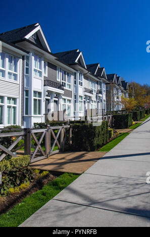 Row of new townhomes in a sidewalk neighborhood. On a sunny day in spring against bright blue sky. Stock Photo