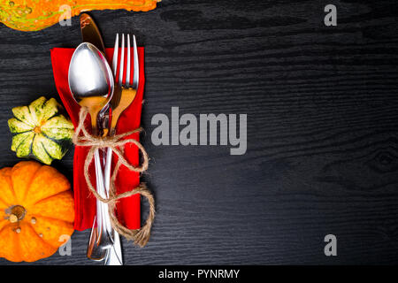 Autumn background from pumpkins, spoon, fork, knife set with thread bow, vintage place setting on black wooden table. Thanksgiving day concept Stock Photo