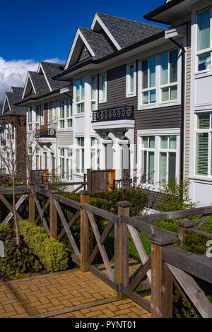 Row of new townhomes in a sidewalk neighborhood. On a sunny day in spring against bright blue sky. Stock Photo