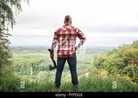 Rear view of lumberjack in forest holding an axe on his shoulder Stock Photo