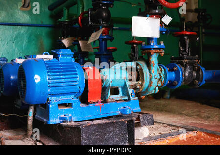 Old, rusty scratches water pump with an electric motor dyed in blue color on the cold water pipe. Stock Photo