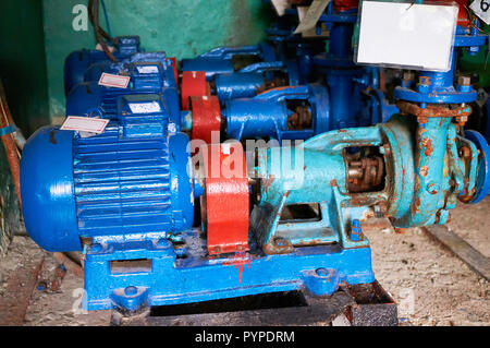 Old, rusty scratches water pump with an electric motor dyed in blue color on the cold water pipe. Stock Photo