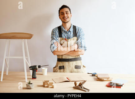 Confident young woodworker standing next to workbench in his carpentry workshop Stock Photo