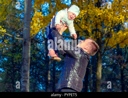 dad holds a girl in his arms raised above the sky Stock Photo