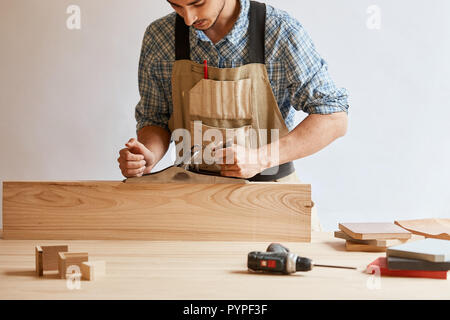carpenter working with wood using plane against white wall in studio. Stock Photo