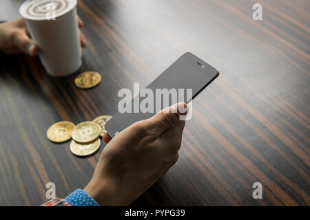 Rich man holding a bitcoin coin and drinking a coffee with a phone and gold coins of bitcoin on a table. Profit from mining of bitcoins. Stock Photo