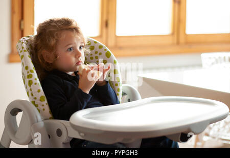 Little girl eats bread in the high chair. Stock Photo