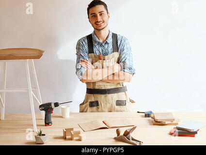 Confident young woodworker standing next to workbench in his carpentry workshop Stock Photo