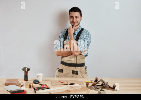 Confident young woodworker standing next to workbench in his carpentry workshop Stock Photo