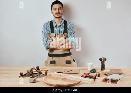 Confident young woodworker standing next to workbench in his carpentry workshop Stock Photo
