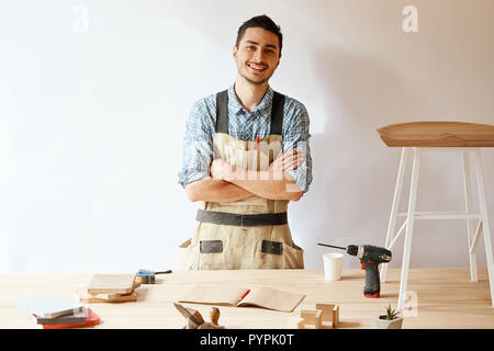 Confident young woodworker standing next to workbench in his carpentry workshop Stock Photo