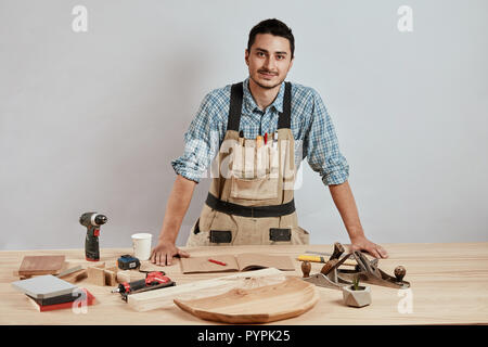Confident young woodworker standing next to workbench in his carpentry workshop Stock Photo