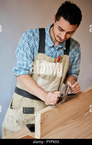 carpenter working with wood using plane against white wall in studio. Stock Photo