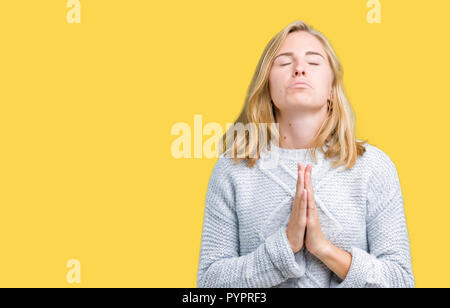 Beautiful young woman wearing winter sweater over isolated background begging and praying with hands together with hope expression on face very emotio Stock Photo