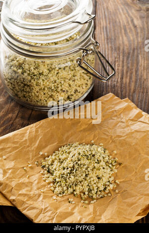 Heap of raw, organic hemp seeds on brown paper with hemp seeds in storage jar on rustic table background Stock Photo