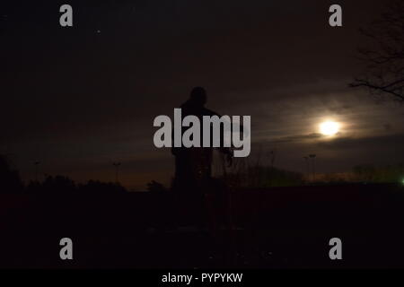 Timeline of the rising moon during the night  dusk sky viewed from a Bronze sculpture silhouette in the military cemetery Reimsbach an der Saar Germany Stock Photo