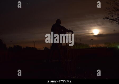 Timeline of the rising moon during the night  dusk sky viewed from a Bronze sculpture silhouette in the military cemetery Reimsbach an der Saar Germany Stock Photo