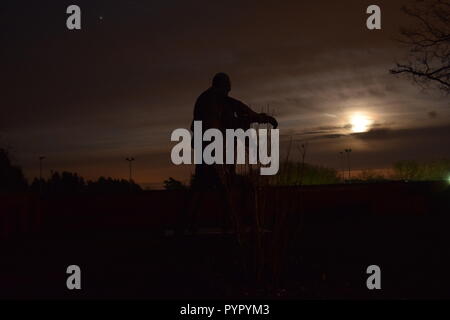 Timeline of the rising moon during the night  dusk sky viewed from a Bronze sculpture silhouette in the military cemetery Reimsbach an der Saar Germany Stock Photo