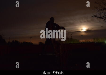 Timeline of the rising moon during the night  dusk sky viewed from a Bronze sculpture silhouette in the military cemetery Reimsbach an der Saar Germany Stock Photo