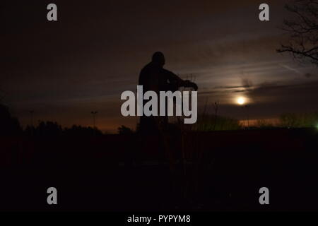 Timeline of the rising moon during the night  dusk sky viewed from a Bronze sculpture silhouette in the military cemetery Reimsbach an der Saar Germany Stock Photo