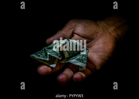 Rumpled one dollar bill in the hand of a person isolated on black. Concept of begging for leaving, poor person, small wage, donations. Stock Photo