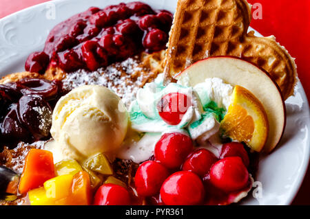 Colorful plate of freshly made waffles with fresh plums, raspberries, cranberries and vanilla ice cream. Stock Photo