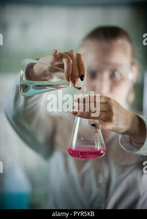 Chemical laboratory. Young blonde woman pouring a blue liquid into the pink. Stock Photo
