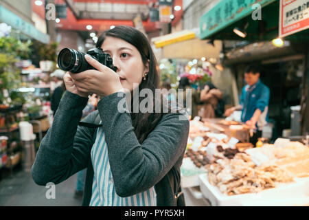 tourist photographer taking picture of local market lifestyle in kuromon market. male shopkeeper in the background. teeming traditional street in jp. Stock Photo