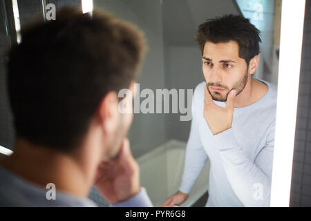 Handsome man touching beard and looking into mirror Stock Photo