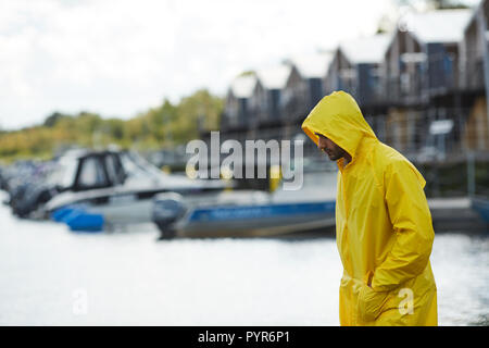 Sad fisherman in yellow waterproof coat moving along pier Stock Photo