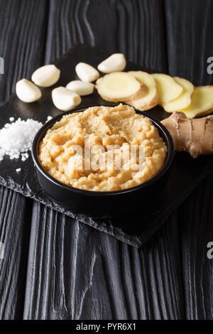 Aromatic freshly prepared ginger garlic paste for Asian cuisine close-up on a black wooden table. vertical Stock Photo